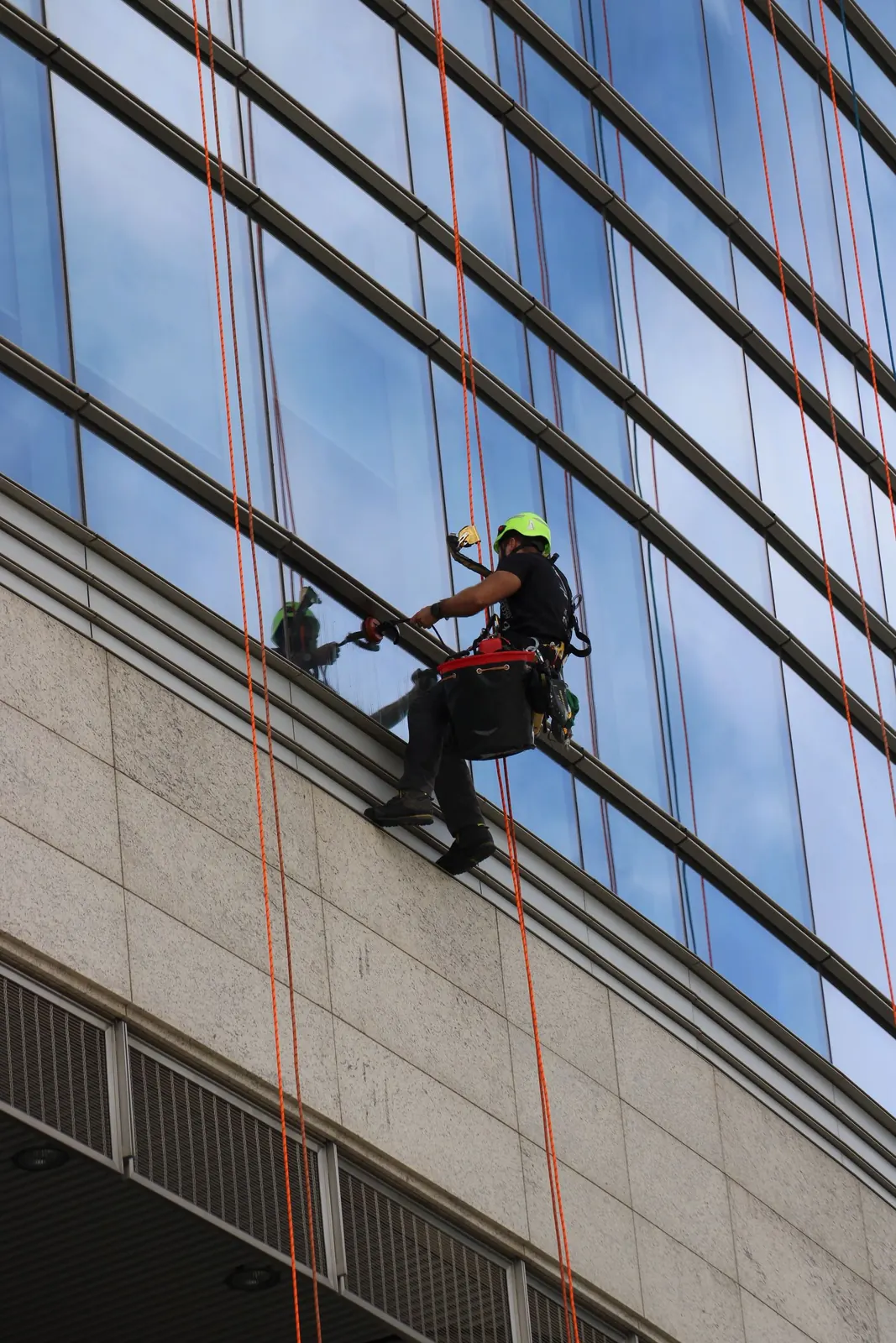 Técnico en altura limpiando cristales y sellando juntas de una fachada